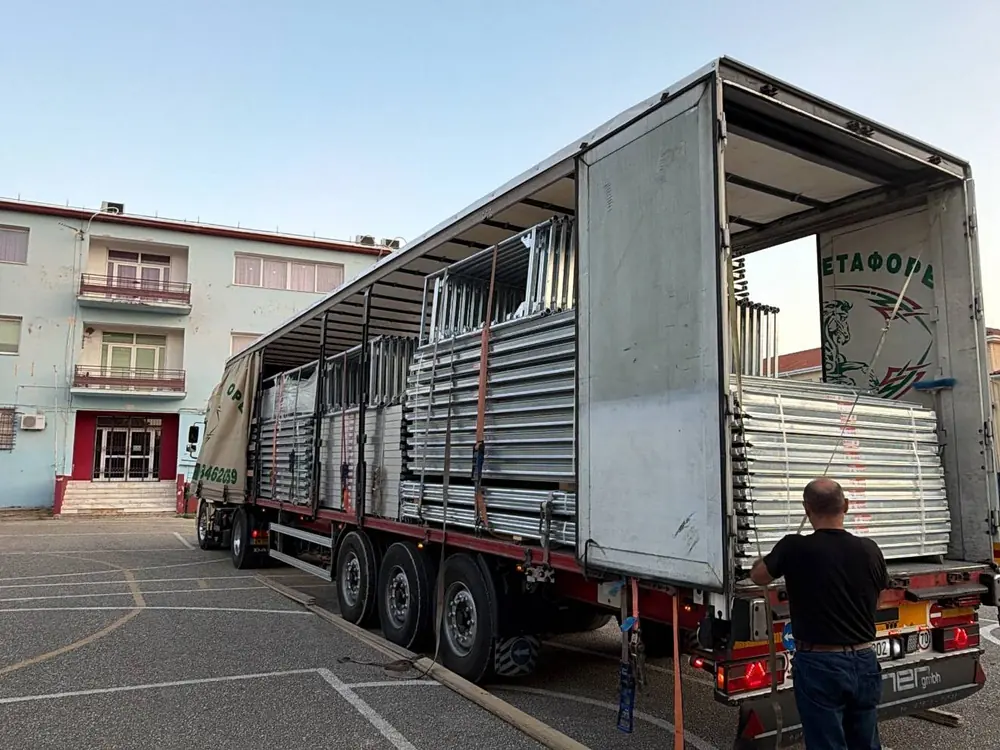 A worker loading scaffolding frames into the side of a curtain-sided truck
